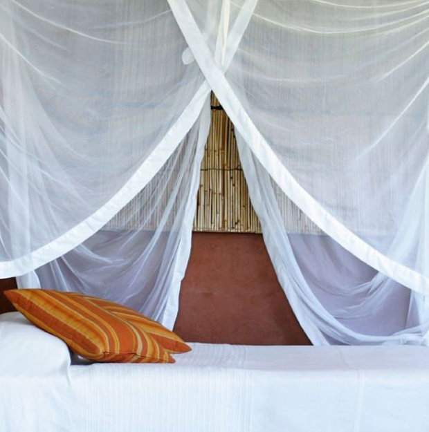 White cotton mosquito net draped over a bed against a terracotta wall